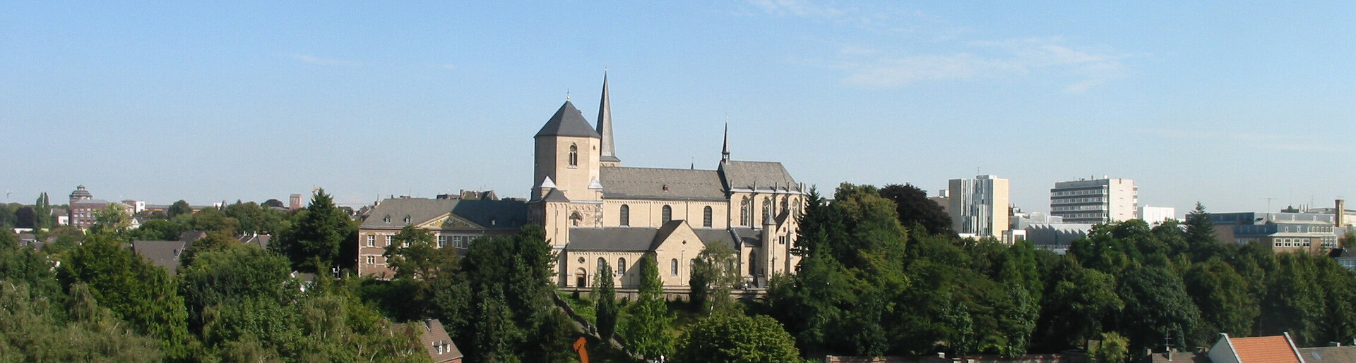 Große Kirche auf bewaldetem Hügel, dahinter Stadtpanorama mit Gebäuden