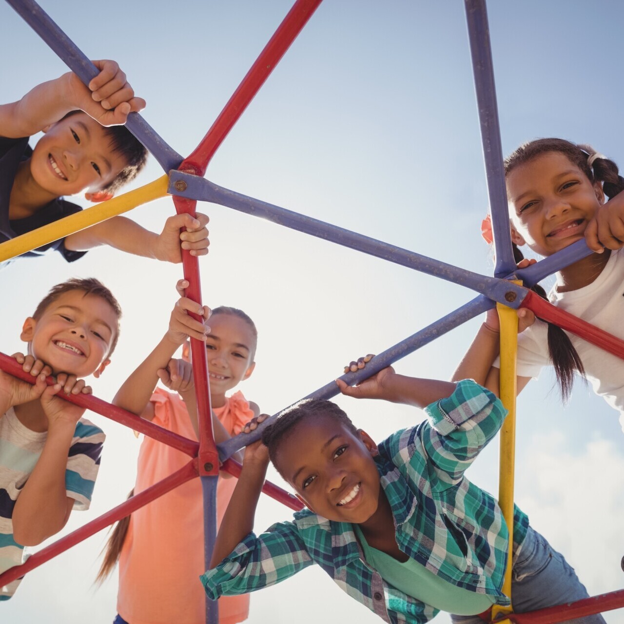 Mehrere lachende Kinder klettern gemeinsam an einem bunten Klettergerüst und schauen fröhlich in die Kamera