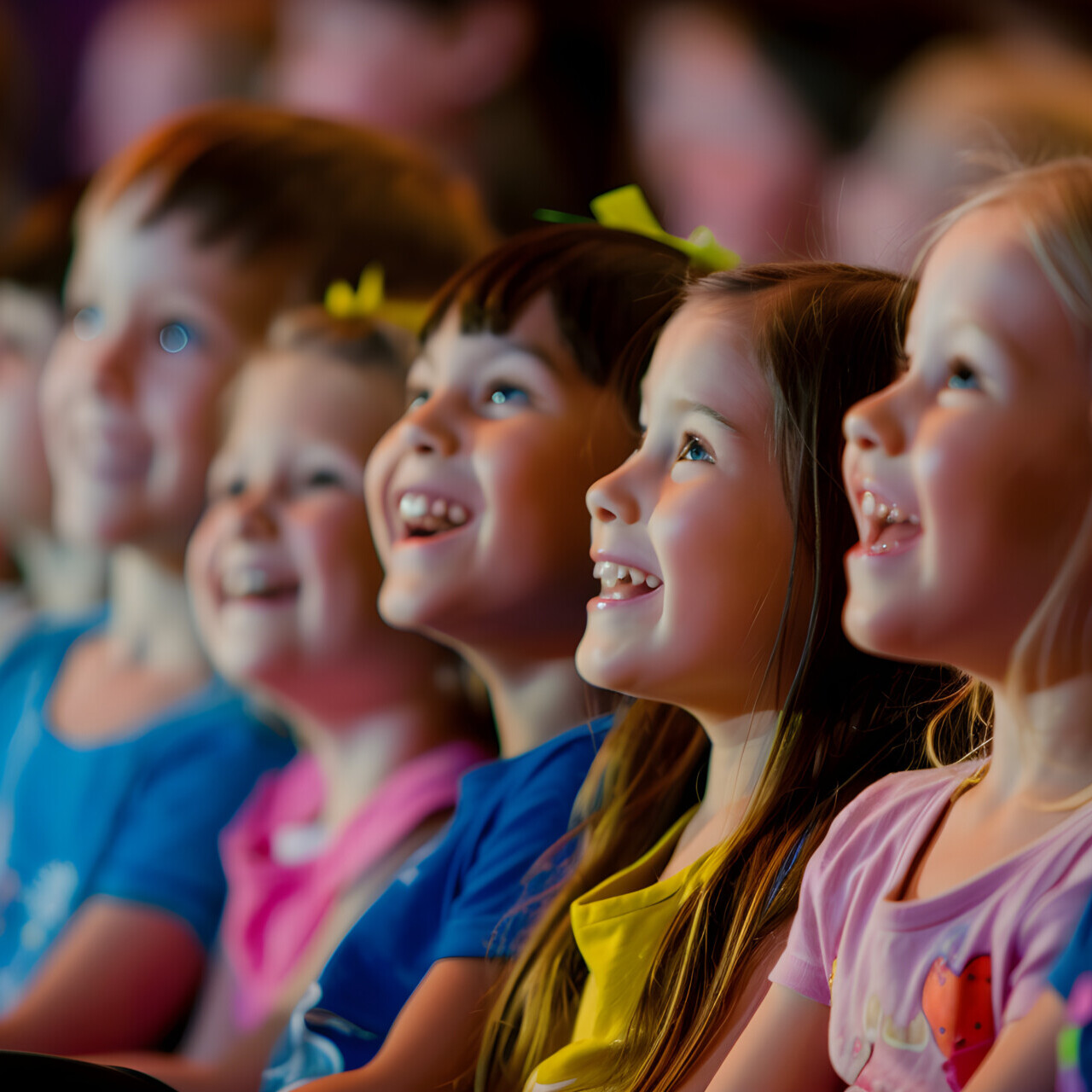 Mehrere lachende Kinder sitzen nebeneinander und blicken aufmerksam sowie begeistert nach vorne.