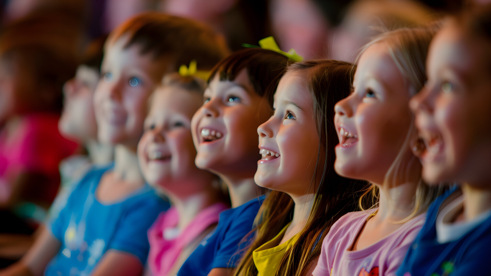 Mehrere lachende Kinder sitzen nebeneinander und blicken aufmerksam sowie begeistert nach vorne.